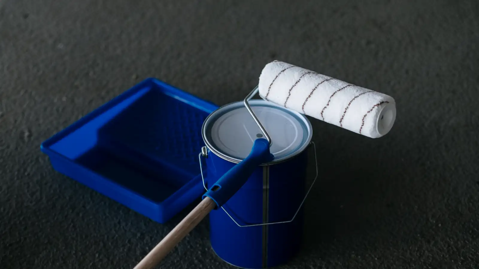 Cubo de pintura y rodillo sobre un suelo de hormigón preparado para pintar